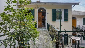 A building with a stone staircase leading to a wooden door, green shutters, and a small outdoor seating area with a table and chairs. - Casa Lucia a Rapallo (Rapallo)