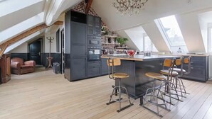 A modern kitchen with a central island, bar stools, and a chandelier.