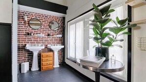 A bathroom with two white sinks, a wooden cabinet, a mirror, and a potted plant by a window.