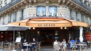 An outdoor seating area of Le Suzy, a cafe with a classic European architectural style, featuring outdoor tables and chairs under a large awning.