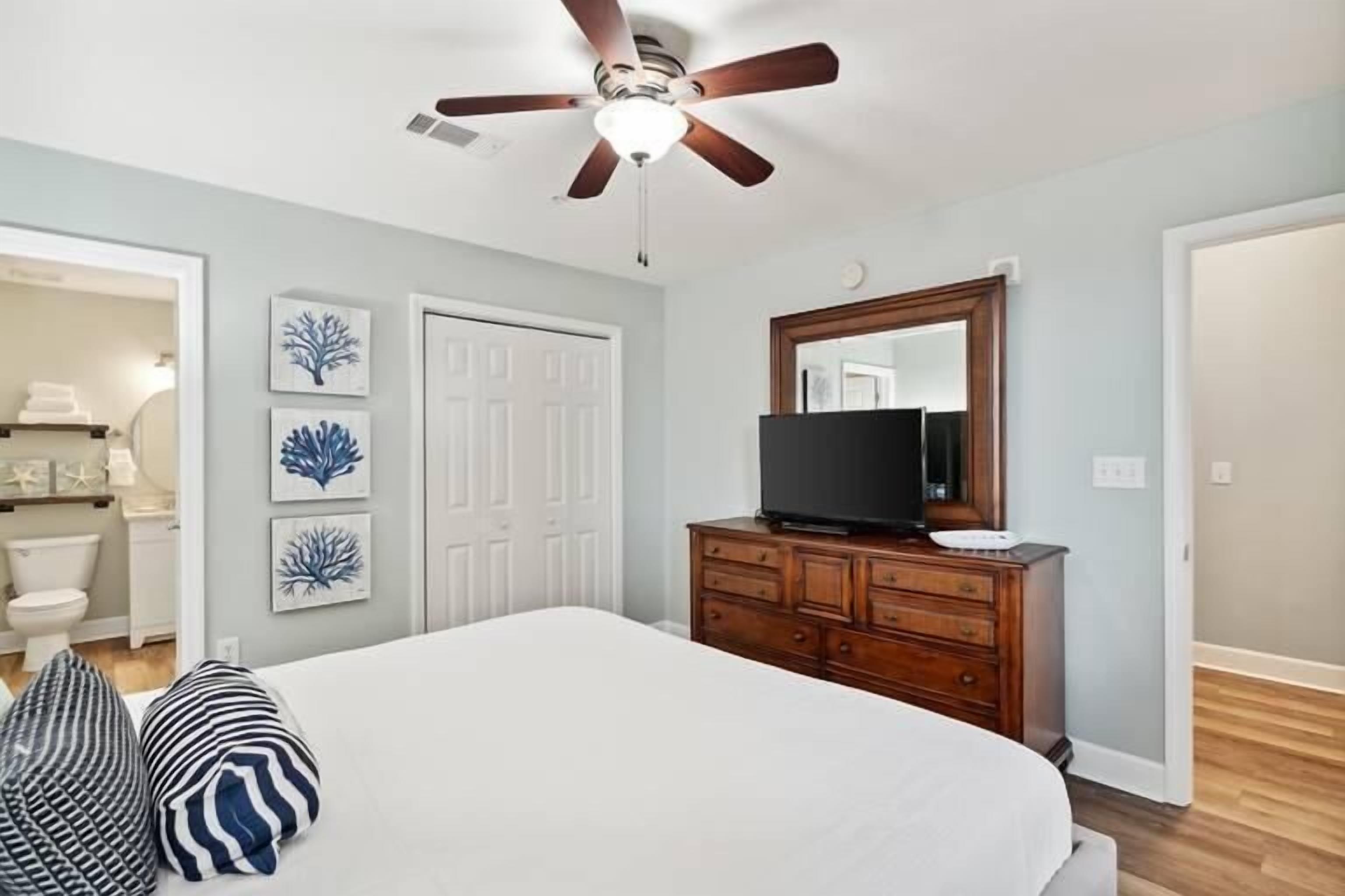 A bedroom with a bed, a ceiling fan, a dresser, and a television.