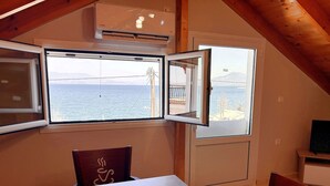 A room with a table and chairs, a window with a view of the sea, and an air conditioning unit. - Bella Vista Junior in Kamena Vourla (Kamena Vourla)