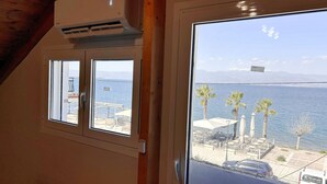 A room with a large window overlooking a body of water, a view of the sea, and a mountain range in the distance. - Bella Vista Junior in Kamena Vourla (Kamena Vourla)