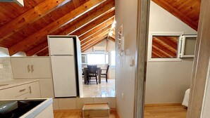 A compact kitchen with wooden beams, a refrigerator, and a dining area with chairs. - Bella Vista Junior in Kamena Vourla (Kamena Vourla)