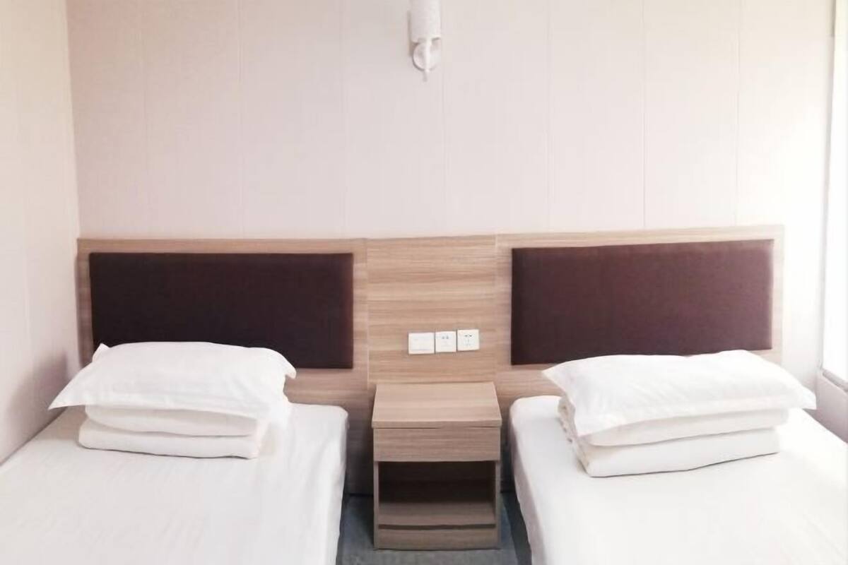 A hotel room with two beds, a wooden headboard, a small bedside table, and a wall-mounted light fixture.