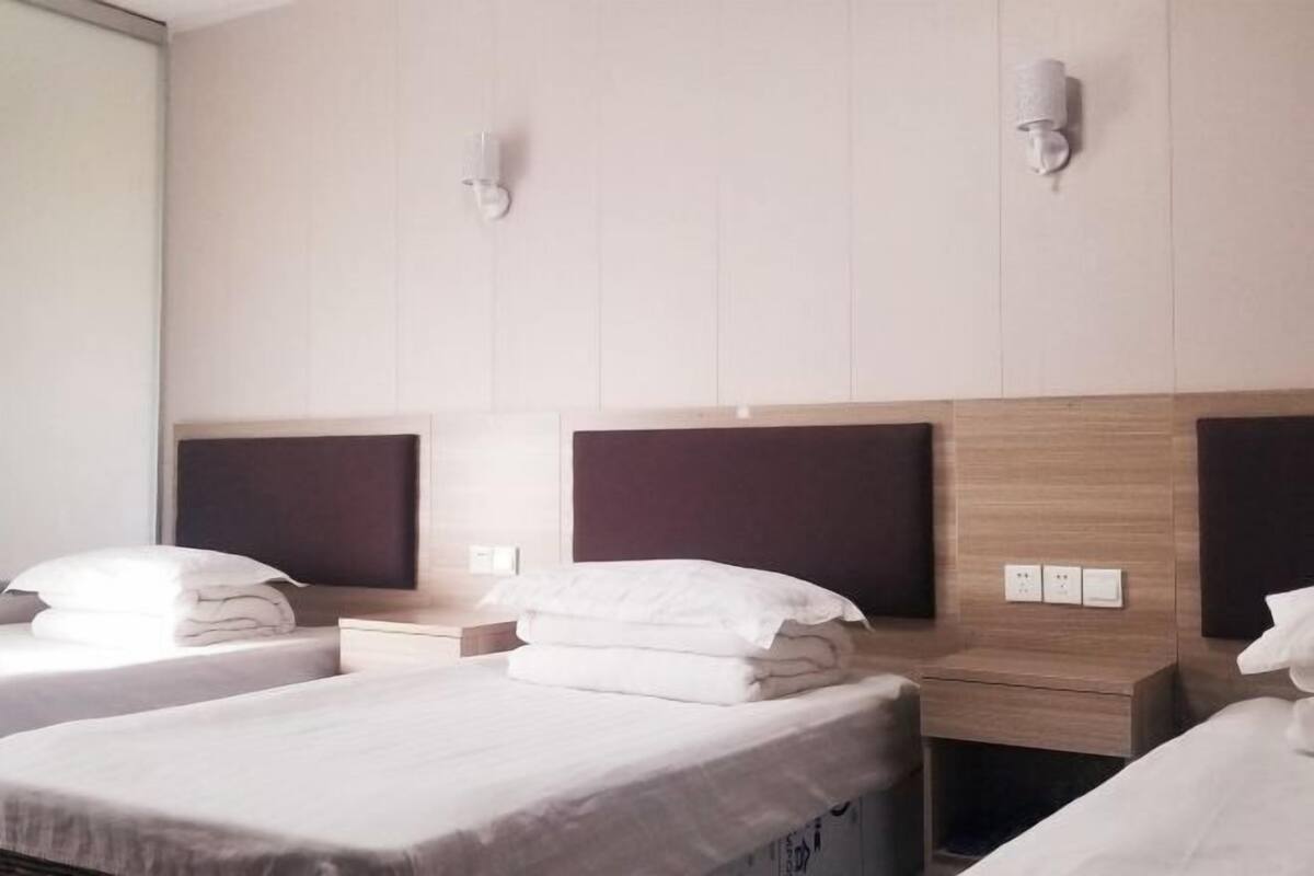 A hotel room with two beds, a wooden headboard, a nightstand, and a wall-mounted light fixture.