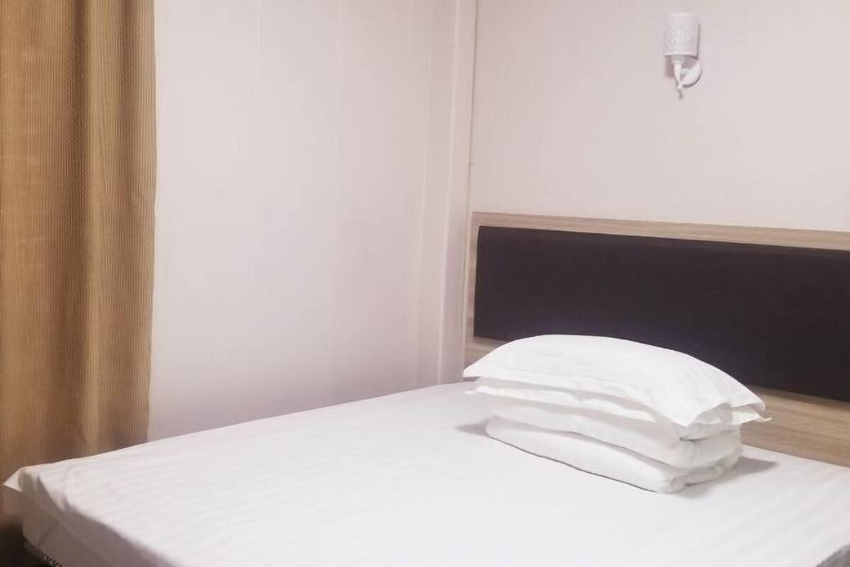 A hotel room with a bed, a headboard, a wall-mounted light, and a curtain.
