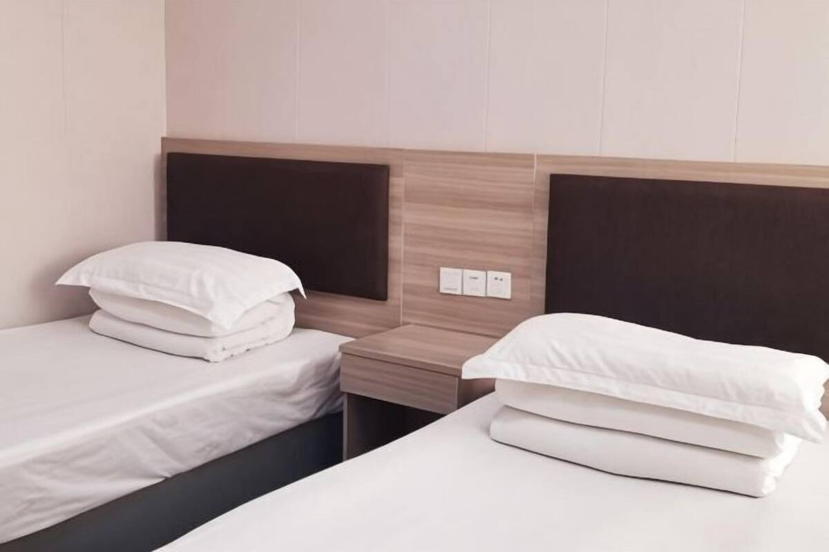 A hotel room with two single beds, a wooden headboard, a bedside table, and a power outlet.