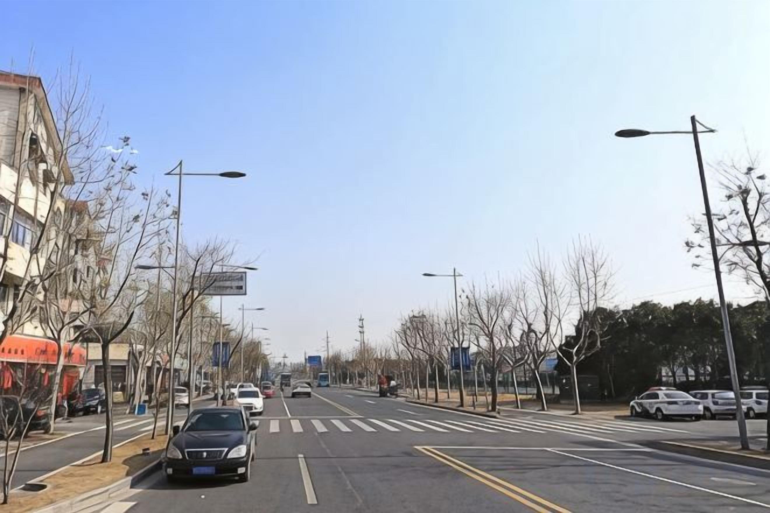 A wide urban street with buildings on both sides, clear skies, and a few cars on the road.