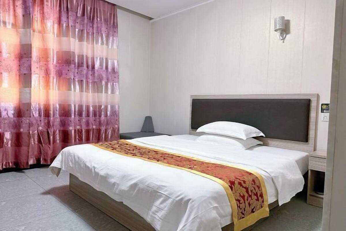 A hotel room with a bed, a nightstand, a lamp, and a curtain.
