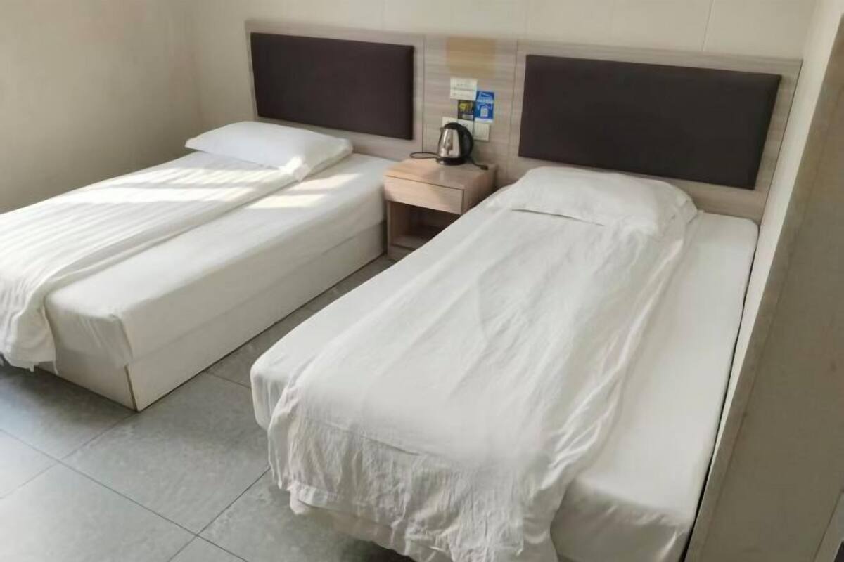 A hotel room with two single beds, a bedside table with a kettle, and a small cabinet.