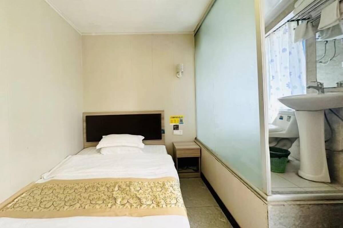 A small hotel room with a single bed, a nightstand, a mirror, and a bathroom with a sink and toilet.