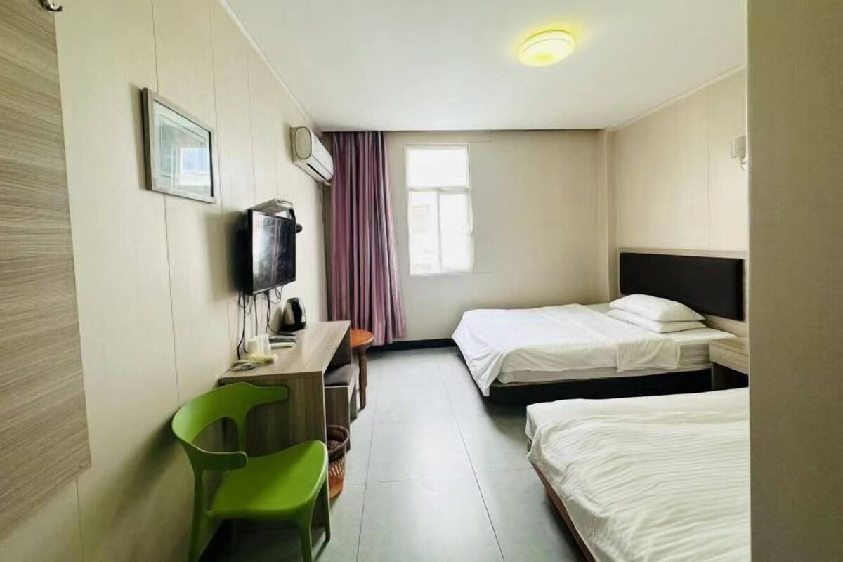 A hotel room with two beds, a desk, a chair, a television, and a window with curtains.