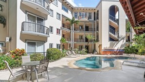 A pool area with lounge chairs and a table, surrounded by multi-story buildings with balconies. - 3-BD Beauty with Pool Near Beach (Tempate)