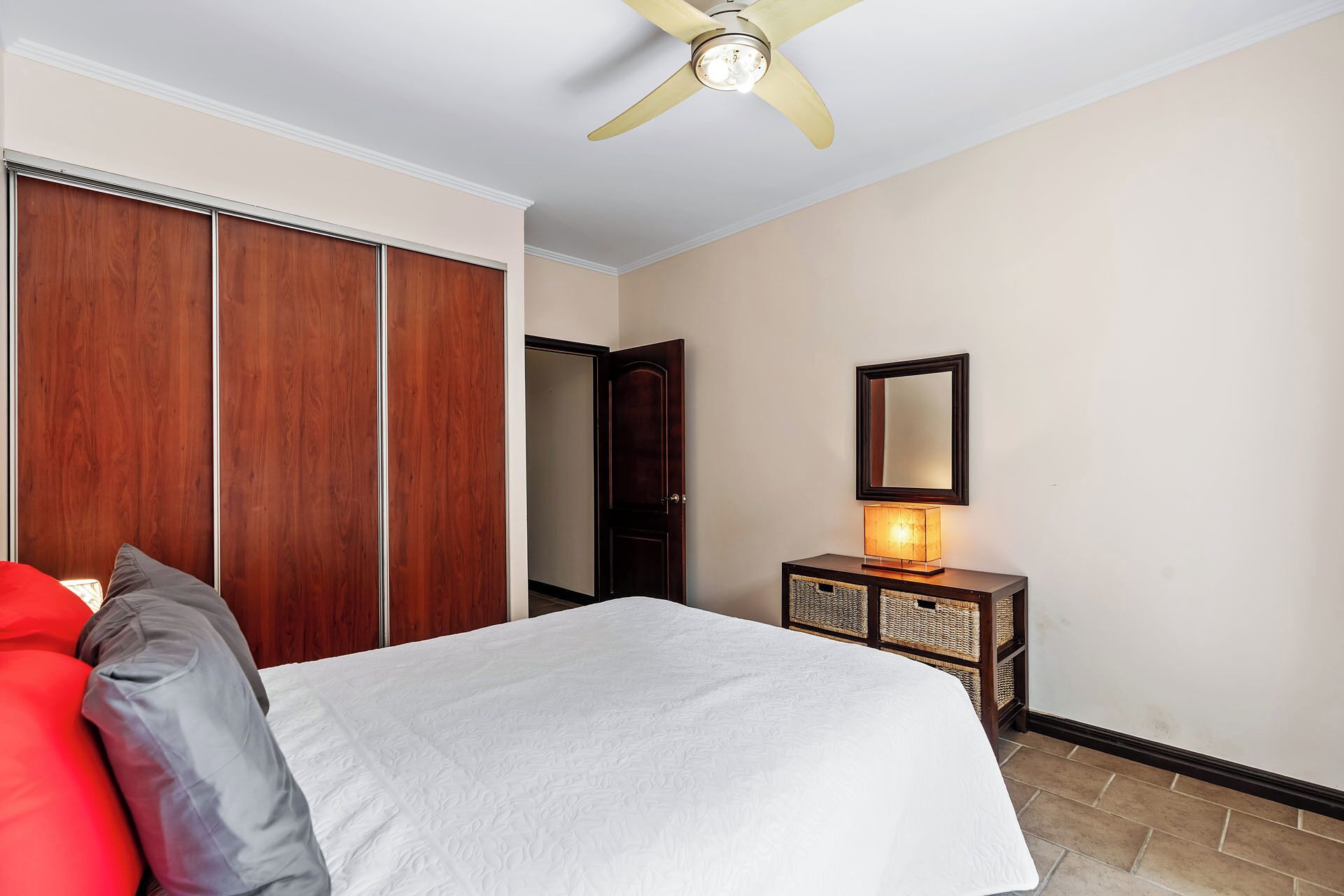 A bedroom with a bed, a wardrobe, a mirror, and a bedside table with a lamp.