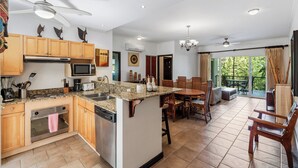 A spacious kitchen with granite countertops, wooden cabinets, and a central island. There is a dining area with a table and chairs, and a balcony with a view of the outdoors. - 3-BD Beauty with Pool Near Beach (Tempate)