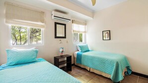 A bedroom with two beds, an air conditioner, a ceiling fan, and a window with a view of trees. - 3-BD Beauty with Pool Near Beach (Tempate)