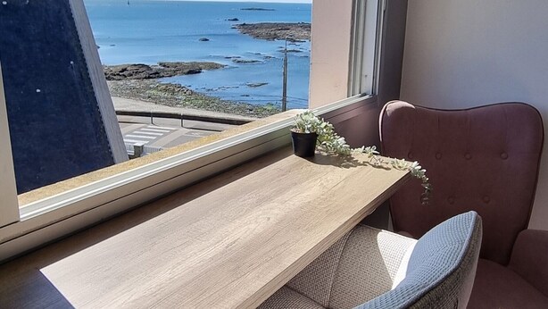 Ein Zimmer mit einem Holztisch, einem Laptop und Meerblick durch ein Fenster.