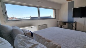 Ein Hotelzimmer mit Bett, Schreibtisch, Stuhl, Fernseher und einem Fenster mit Blick auf Gebäude.