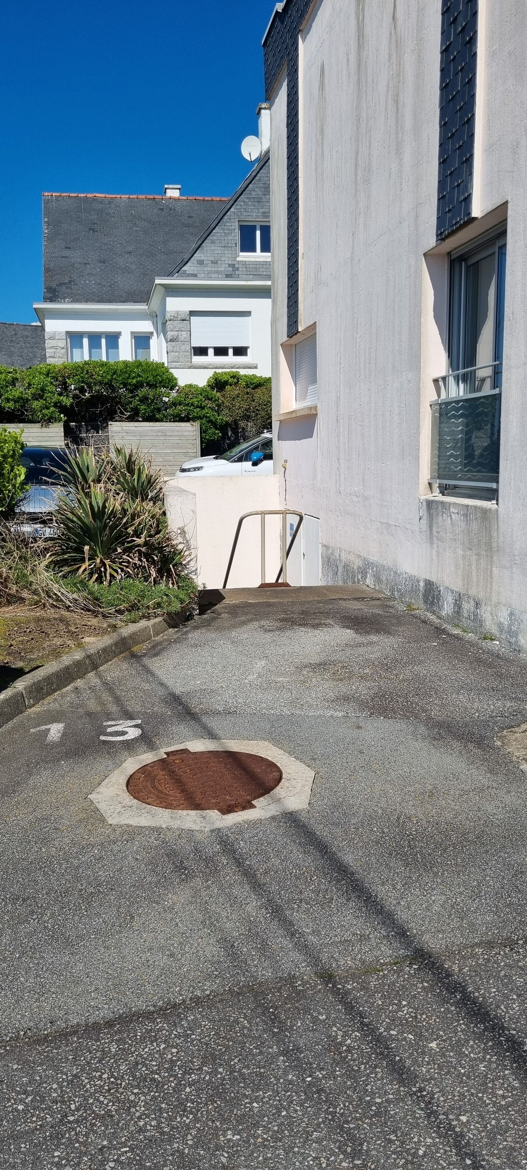 A residential street with houses, a manhole cover, and a clear blue sky.