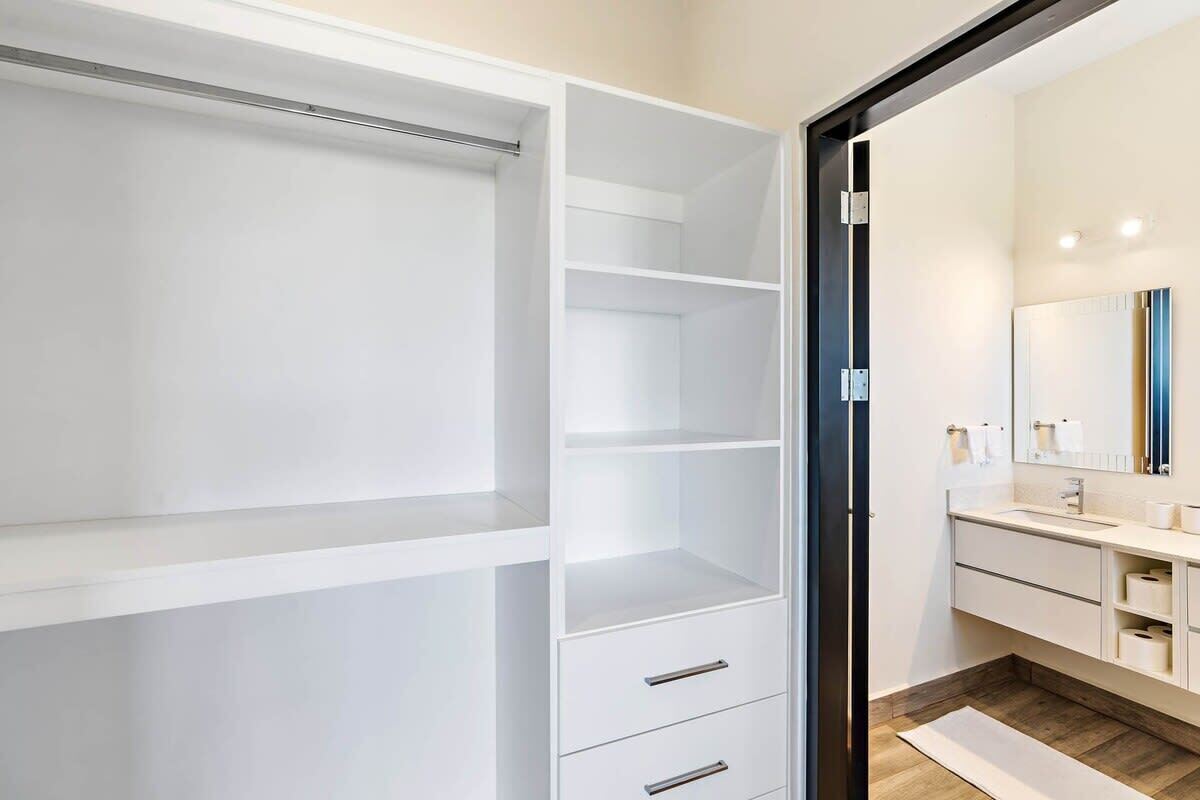A modern bathroom with a large mirror, white cabinetry, and a wooden floor.