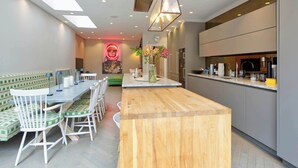 A modern kitchen with a wooden island, a dining area with green and white chairs, and a neon art piece on the wall. - Elegant 4 Bedroom House - Clapham (London)