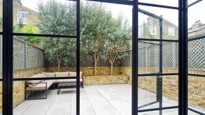 A patio with a sofa and a table, surrounded by a brick wall and a wooden fence. - Elegant 4 Bedroom House - Clapham (London)