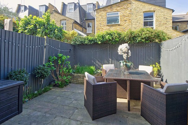 Enjoy outdoor dining or relaxation on the patio, surrounded by lush greenery and a charming brick backdrop.