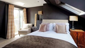 Een hotelkamer met een groot bed, een stoel, een houten kast en een raam met gordijnen.