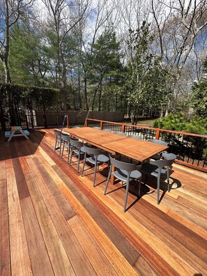 Eine Terrassenausstattung mit Holztisch und -stühlen, umgeben von einem Holzzaun und Bäumen.