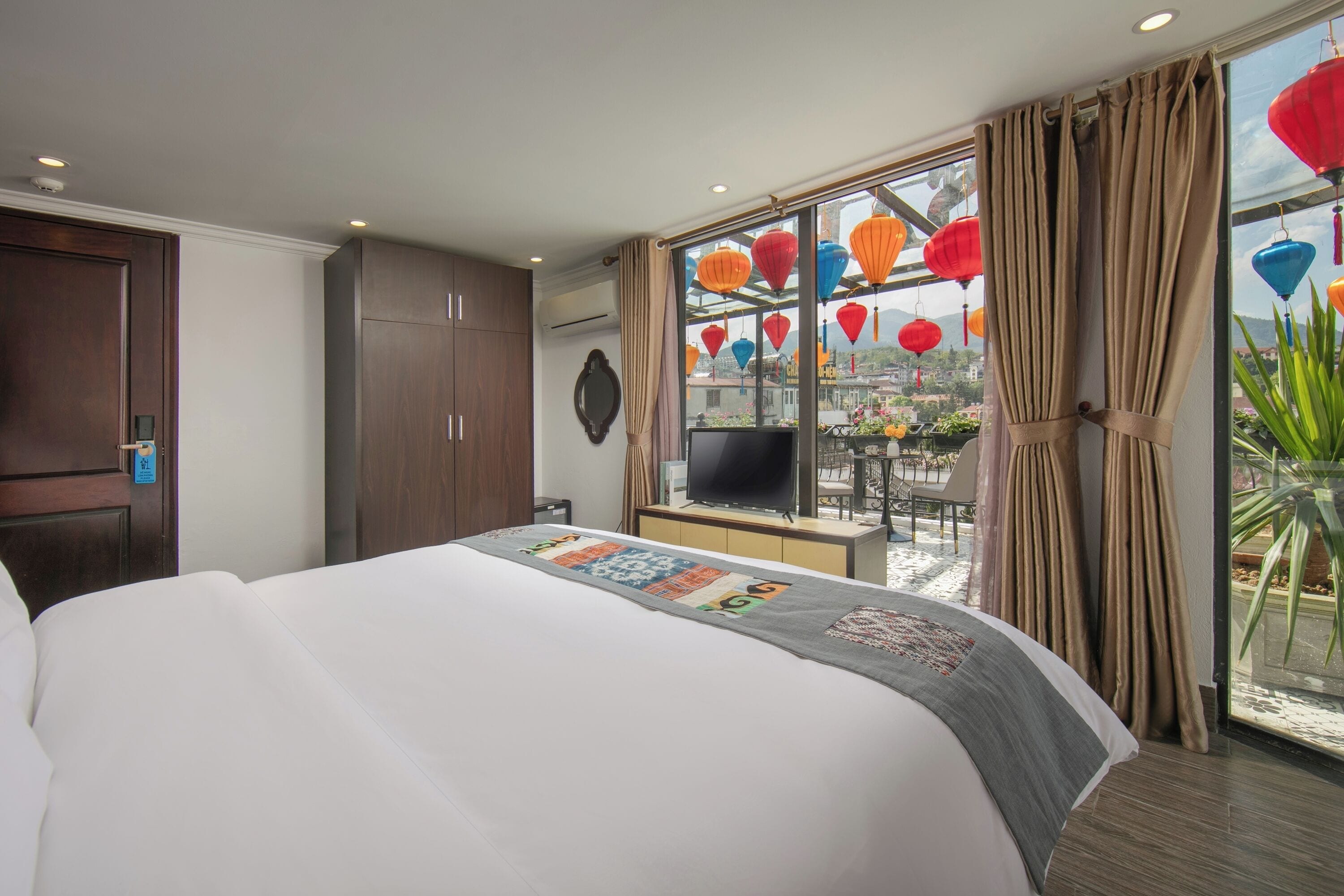 A hotel room with a large bed, a TV, a desk, and a window with curtains.