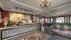 Un área de recepción con un mural de estilo asiático tradicional, una mesa de recepción y un sofá colorido en primer plano.
