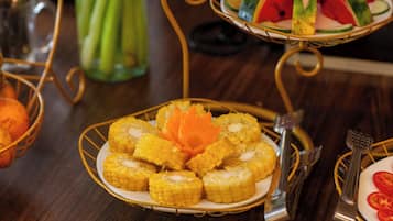 A dining table with a plate of corn on the cob and a basket of oranges.