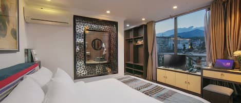 Habitación de hotel con una cama grande, un escritorio con una computadora portátil, un televisor y vistas a las montañas.