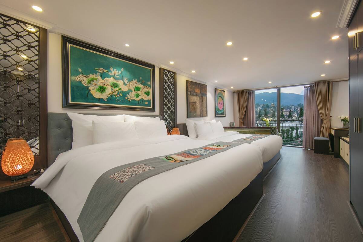 A hotel room with a large bed, a view of the city, and artwork on the walls.