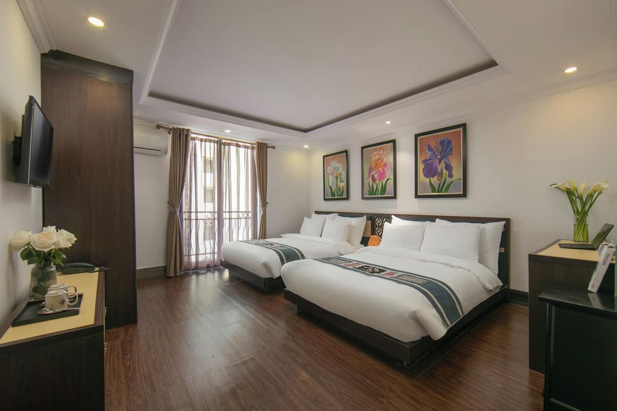 A hotel room with two beds, a TV, a desk, and artwork on the walls.