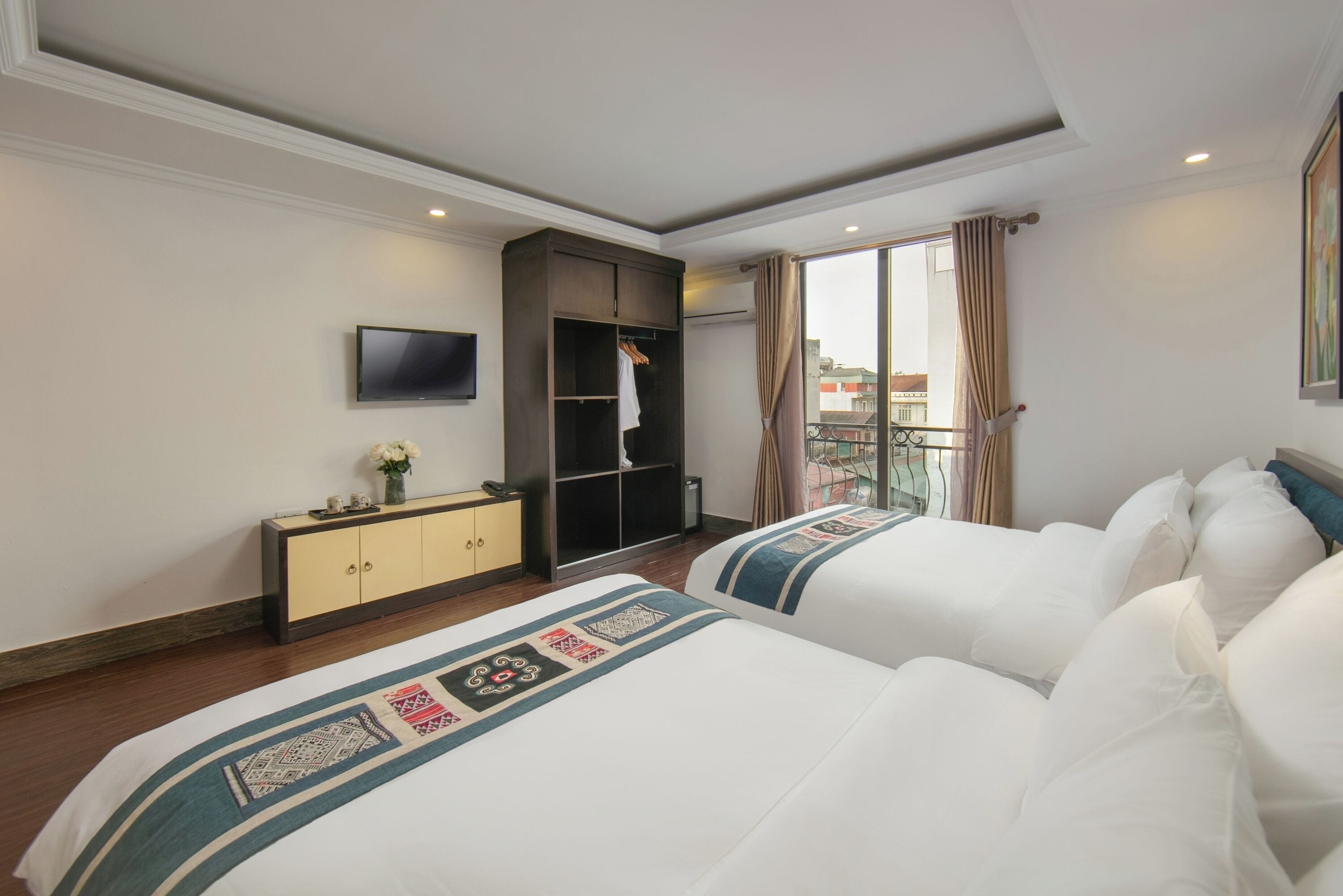 Una camera d'albergo con due letti, un armadio, una televisione e un balcone con vista.