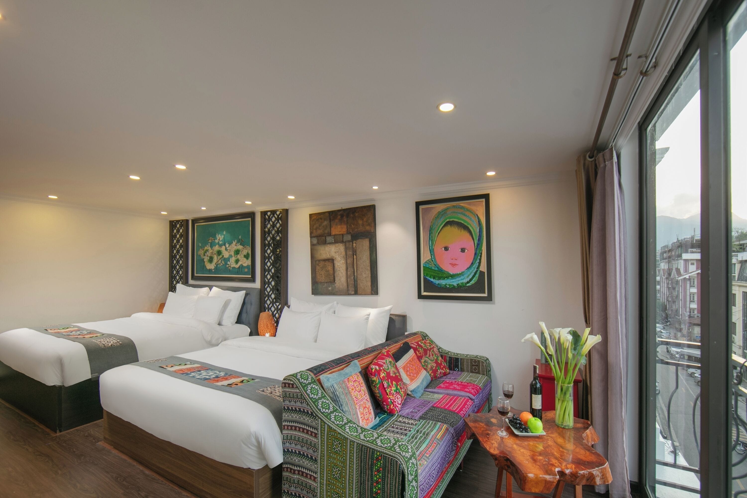 Habitación de hotel con dos camas, un sofá, una mesita con un florero y cuadros en las paredes.