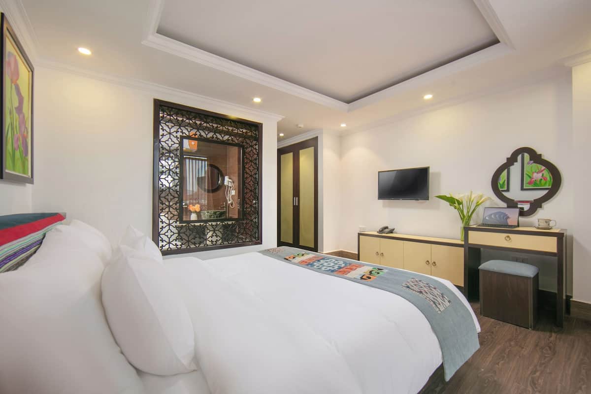 A hotel room with a large bed, a desk with a computer, a TV, and a decorative mirror.