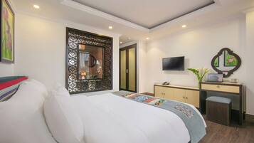A hotel room with a large bed, a desk with a computer, a TV, and a decorative mirror.