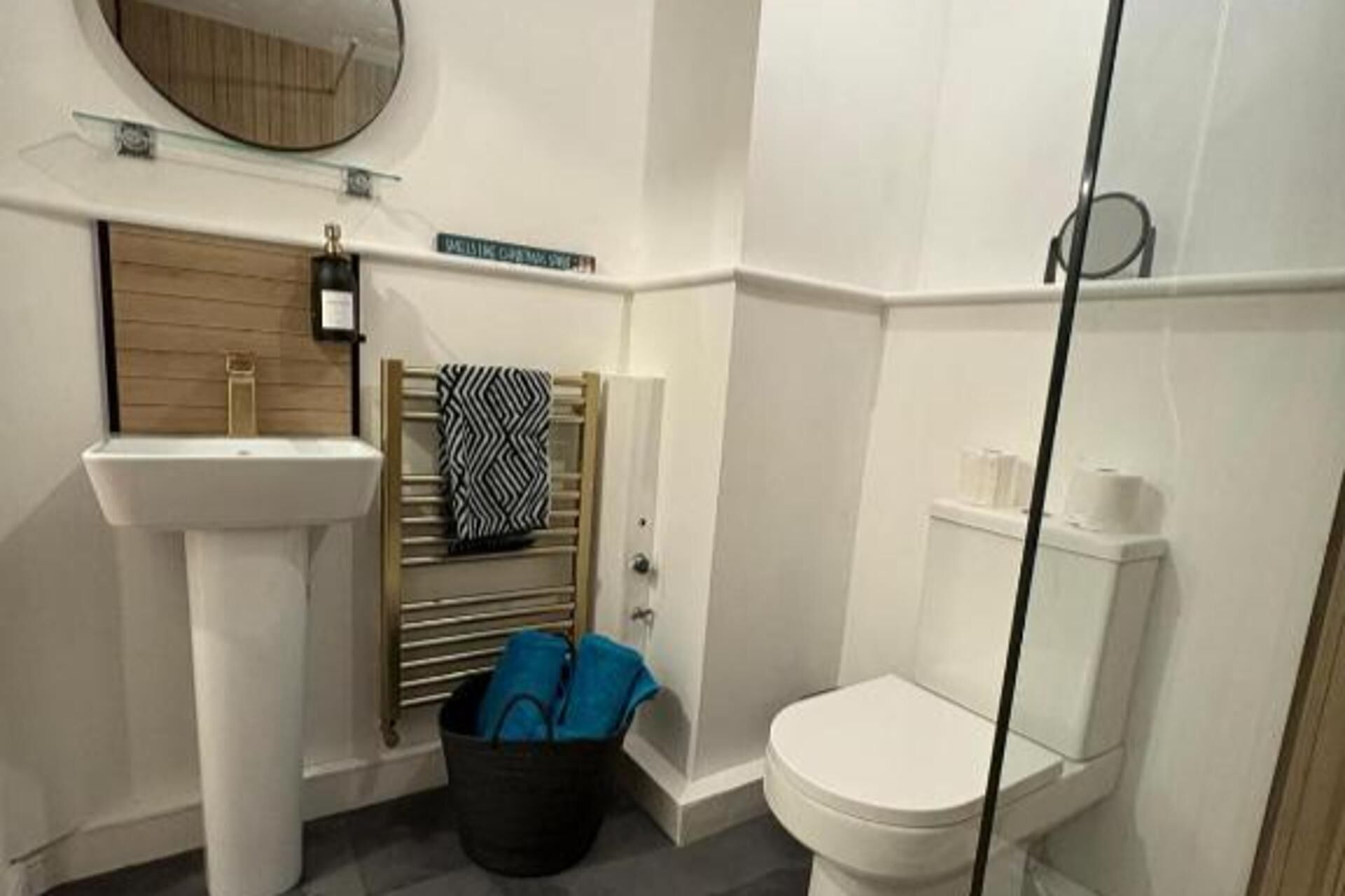 Un bagno con lavabo a piedistallo, un water, zona doccia e portasciugamani con un asciugamano decorato.
