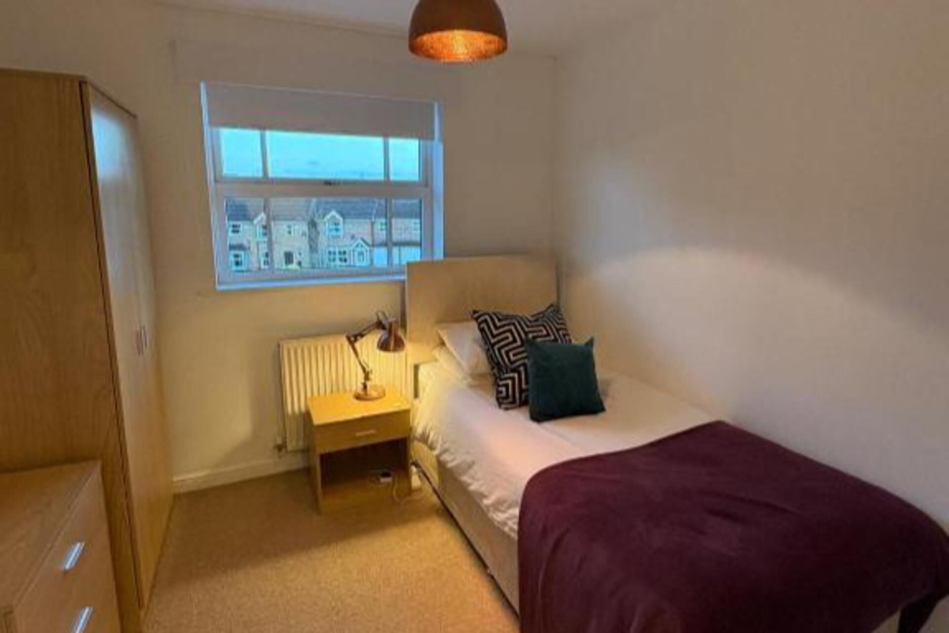 Un dormitorio con cama, ventana, radiador y lámpara.