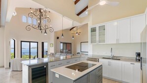 A spacious kitchen with a large island, white cabinetry, and a view of the sea. - Stylish Villa with Brand-New Furniture, Panoramic Ocean Views, and Infinity Swimming Pool & Hot Tub (Potrero)