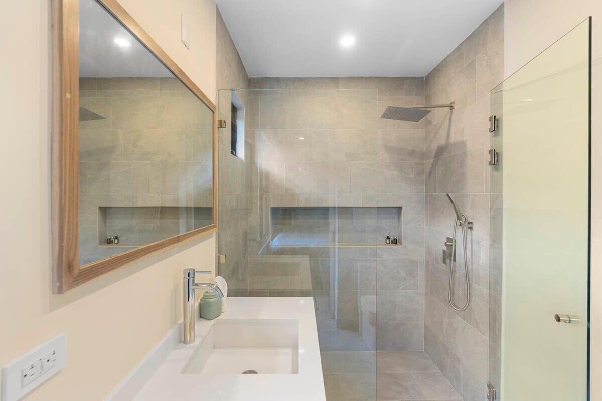 A modern bathroom with a large mirror, a sink, and a shower area.