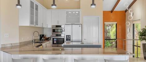 A modern kitchen with a large island, white cabinetry, and pendant lighting.