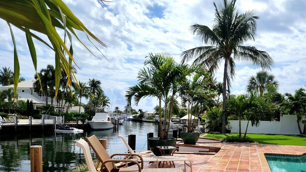 A poolside area with lounge chairs, a tiled deck, and a marina in the background. - Charming waterfront house with 3-bedrooms, 3-full bathrooms and pool (Pompano Beach)