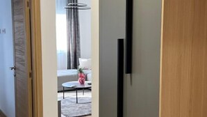 A modern hotel room with a wooden door, a grey wall, and a visible bed in the background.