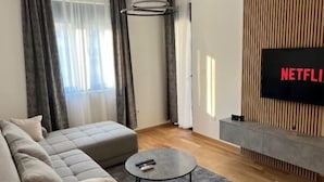 A modern living room with a sectional sofa, a round coffee table, and a flat-screen TV mounted on a wooden panel wall.