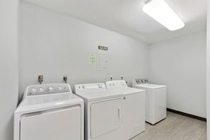 A laundry room with three white washing machines and dryers, a light fixture on the ceiling, and a notice on the wall.