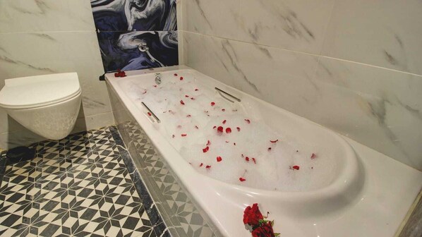 A bathroom with a white bathtub, a toilet, and a patterned floor. - Hotel Sapphire Inn (Thane)